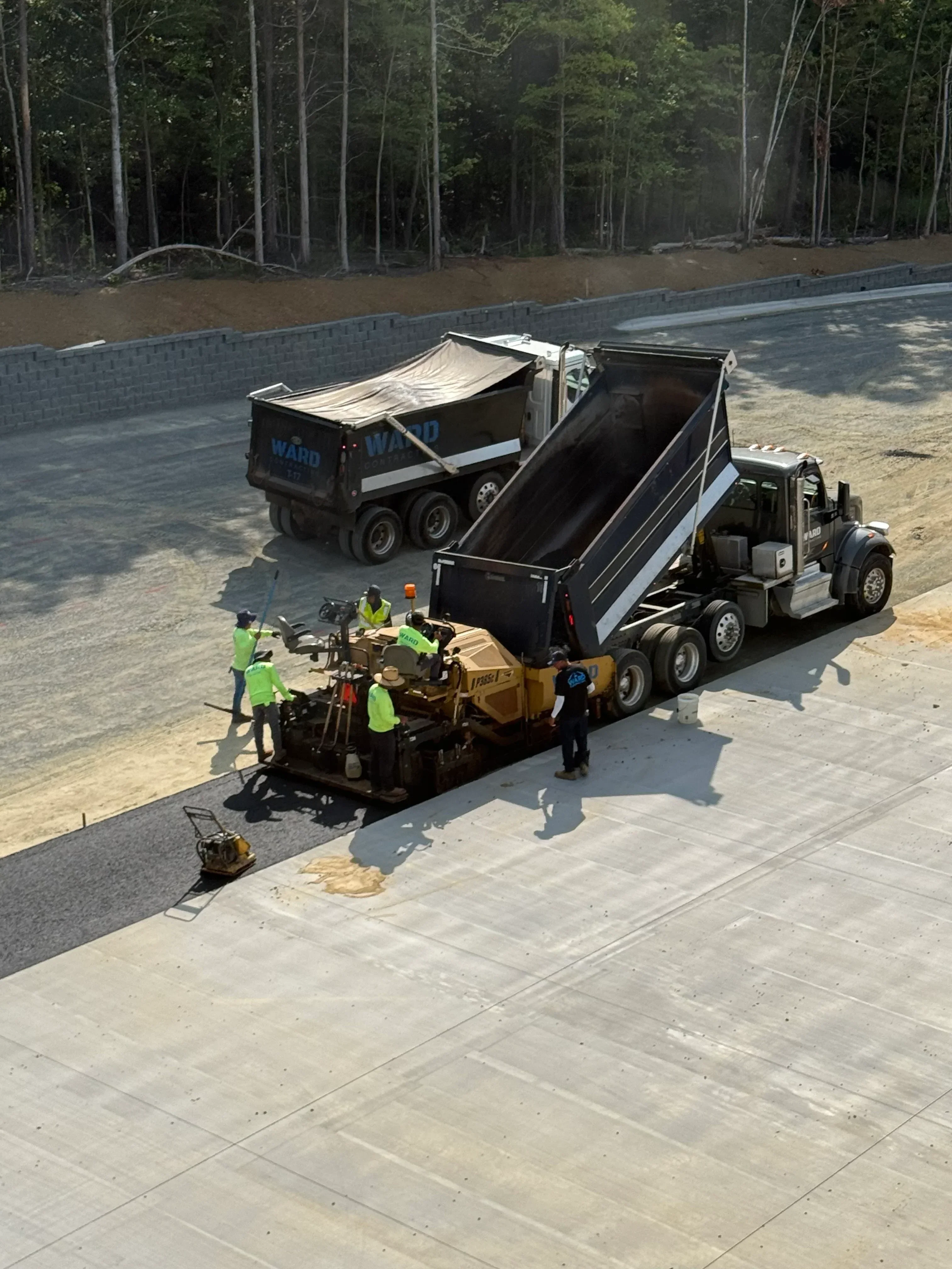 Dump truck and asphalt paving equipment with crew laying fresh asphalt on concrete surface
