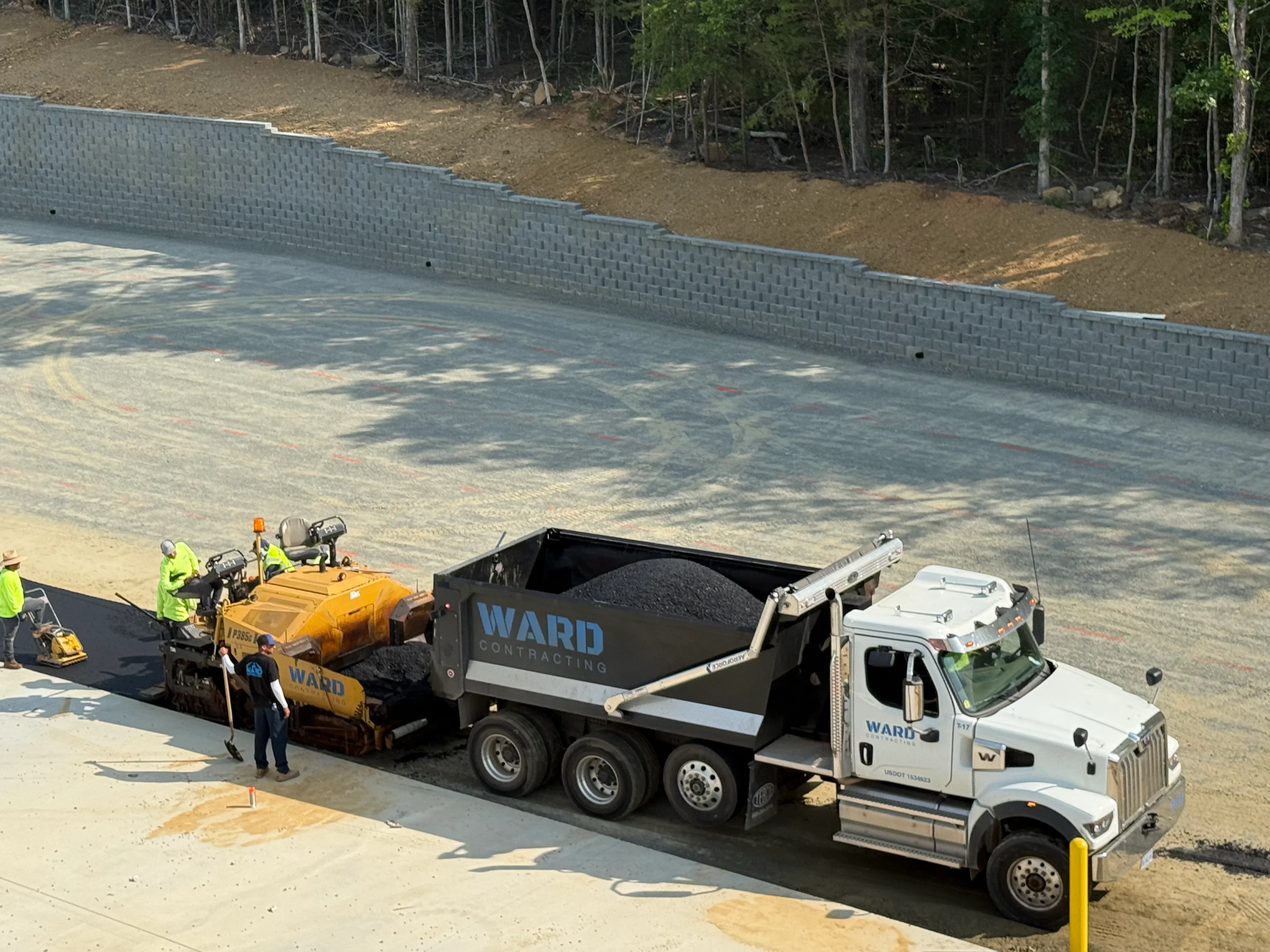 Asphalt paving with segmental block retaining wall, paving equipment and delivery truck on residential site